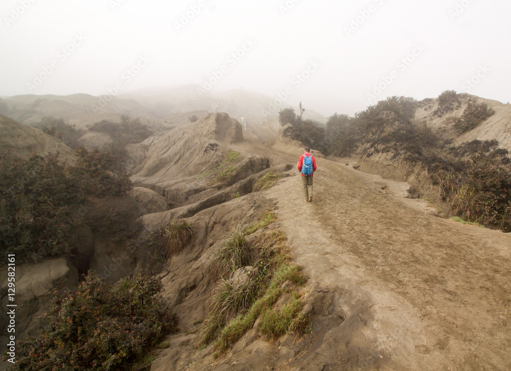 hiker climbs up the side of the Bromo volcano in the fog