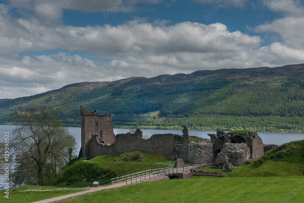 Loch Ness, Scotland - June 2, 2012: The ruins of Urquhart Castle on the green cliffs. Loch Ness visible in back. Green surrounding hills. Dark cloudy sky.