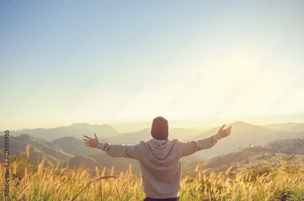 Carefree Happy Man Enjoying Nature on grass meadow on top of mountain cliff with sunrise. Beauty Outdoor. Freedom concept. Sunbeams. Enjoyment. copy space.