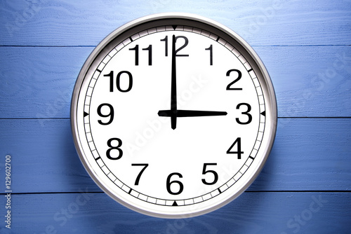 Round clock shows shows at 3 o'clock, clock on blue background