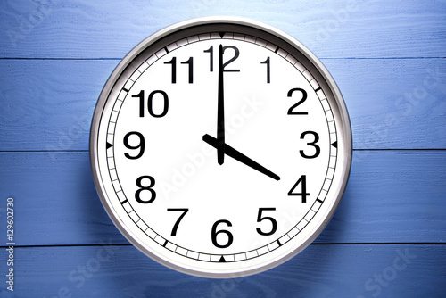 Round clock shows shows at 4 o'clock, clock on blue background