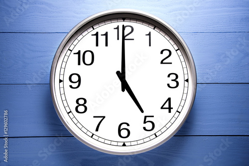 Round clock shows shows at 5 o'clock, clock on blue background