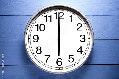 Round clock shows shows at 6 o'clock, clock on blue background