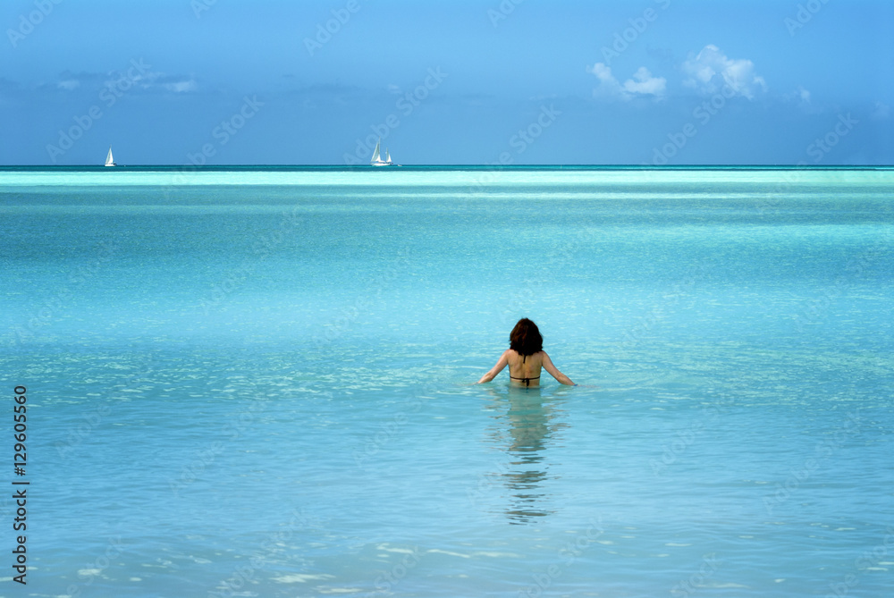 Woman walking into calm ocean waters in tropical island beach scene Woman walking into calm ocean waters in tropical island beach scene