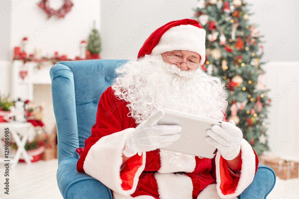 Portrait of happy Santa Claus holding Christmas letter using tab
