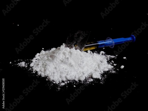 Injection syringe on cocaine drug powder pile on black background