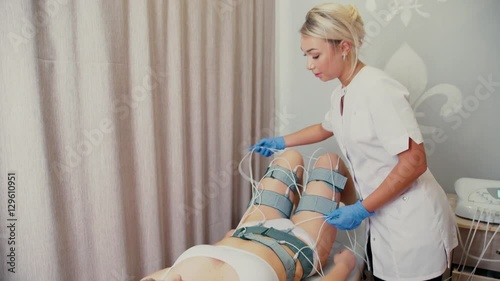 Beautician myostimulator off and helps the patient to knock sensors and remove the wires from the body. Beauty salon. Hardware figure correction. Machine cosmetology. Woman on myostimulation procedure photo