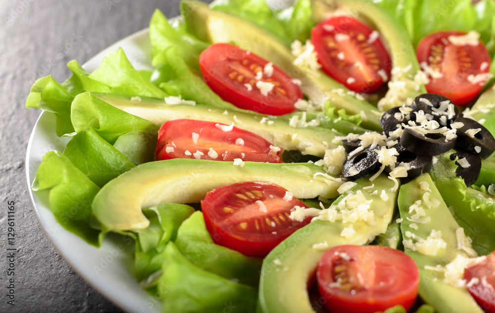 Slices of avocado on salad leaves with cherry tomatoes, grated c Slices of avocado on salad leaves with cherry tomatoes, grated c