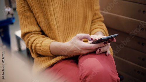 close-up of hands young woman in the orange jacket uses a smartphone, sitting among the things in a shop