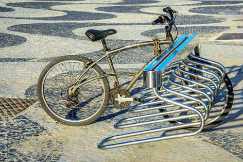 The bicycle parking with one old byke locked via big chain at the Copacabana promenade with its black and white Portuguese pavement design, Rio de Janeiro, Brazil