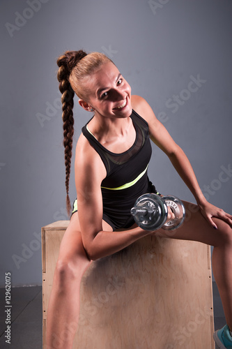 Young confident woman doing biceps curl exercise with dumbbells in fitness center. Slim girl training in the gym with dumbbells photo