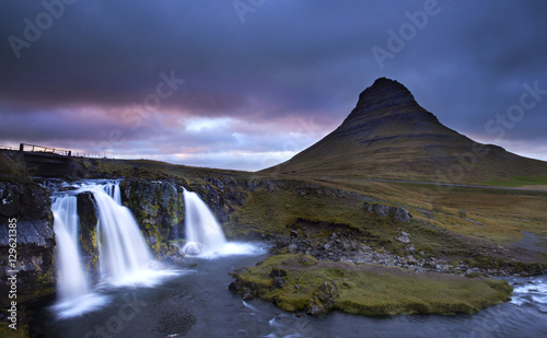 cloudy sunset the top of Kirkjufellsfoss waterfall with Kirkjufell mountain in the background on the north coast of Iceland s Snaefellsnes peninsula taken white a long shutter speed.