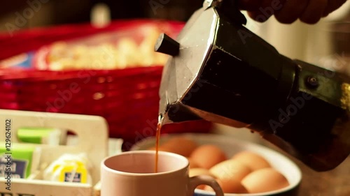 Serving Breakfast. Pouring Steaming Coffee Into a Pink Mug From Black Italian Moka Coffee Pot With Eggs, Bread and Tea in the Background. Close-Up.