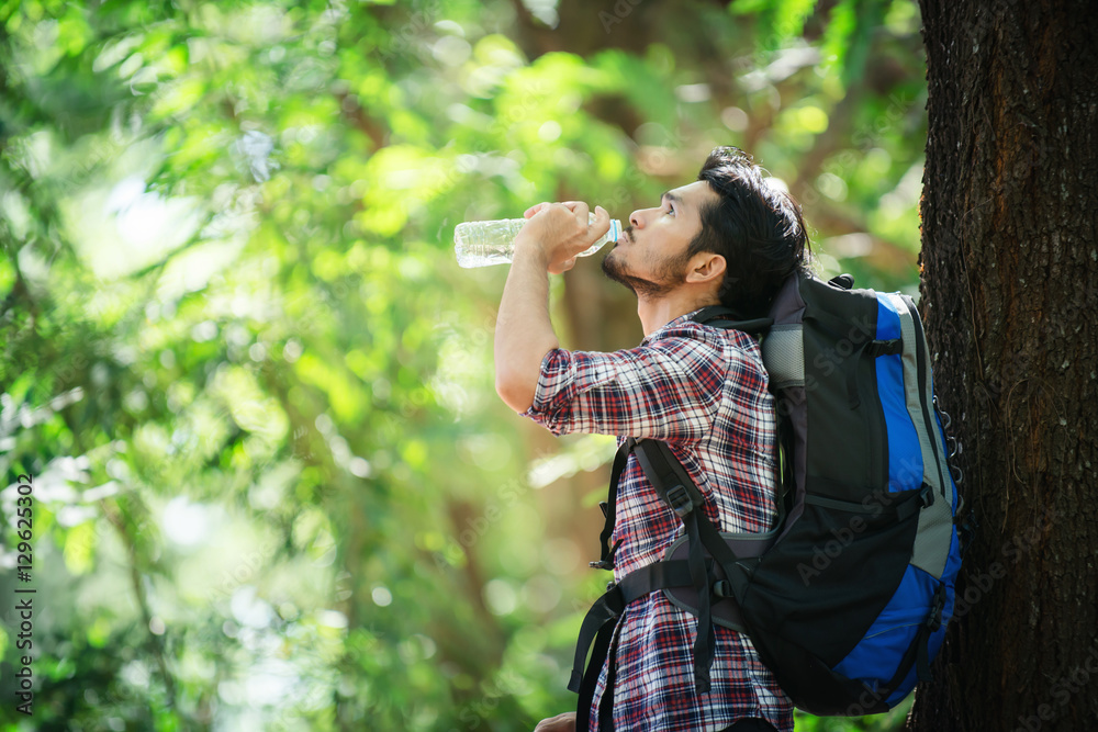 Young man thirsty and drink water during the trek behind a large Young man thirsty and drink water during the trek behind a large