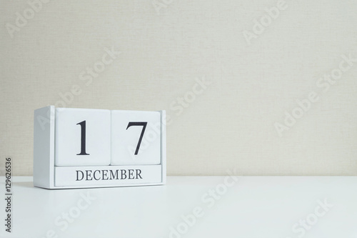 Closeup white wooden calendar with black 17 december word on blurred white wood desk and cream color wallpaper in room textured background with copy space , selective focus at the calendar
