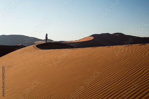 Tourist holding smart phone and taking photo at scenic sand dunes at Sossusvlei, Namib desert, Namib Naukluft National Park, Namibia. Adventure and exploration in Africa.