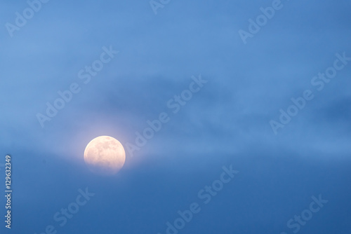 A full moon rises behind a bank of blue clouds © Dan Luchs