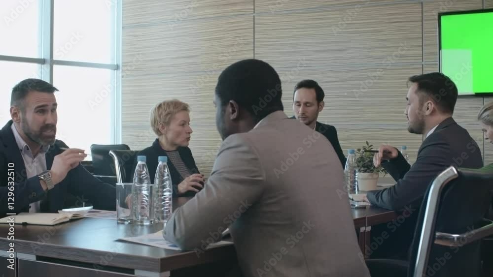 Pan of bearded man sitting behind table in conference room and discussing finances with African businessman