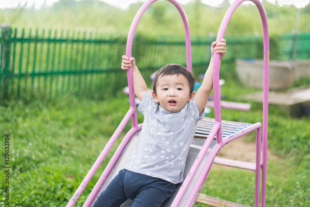 Little Asian kid playing slide at the playground under the sunli Little Asian kid playing slide at the playground under the sunli
