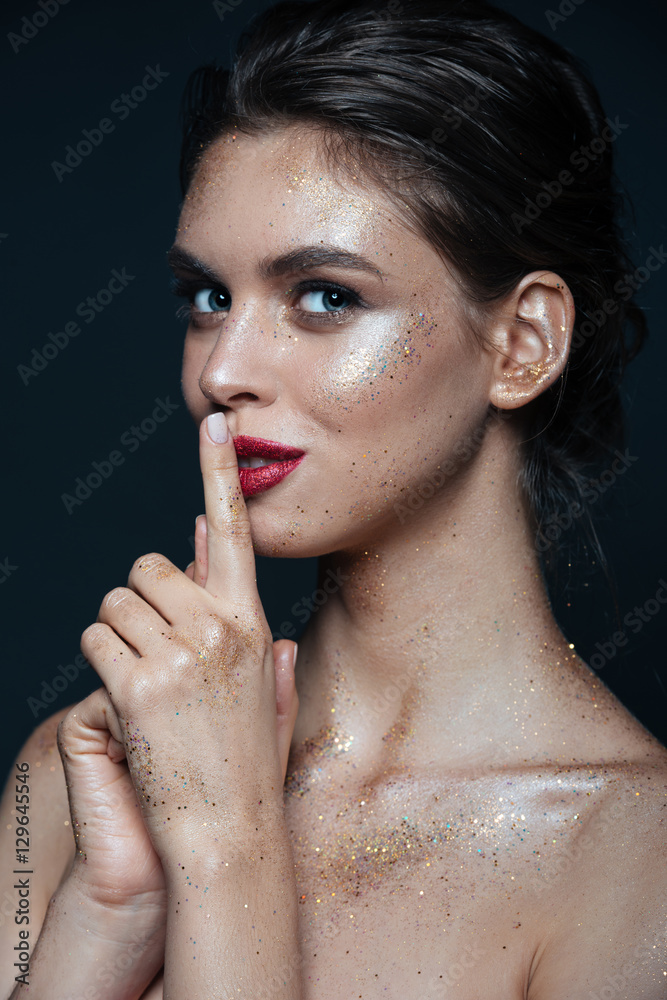 Happy woman with sparkles on her face showing silence sign Happy woman with sparkles on her face showing silence sign