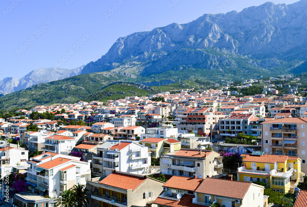 A panoramic view of small coastal town in the summer morning hidden under the mountain peaks. Isolated on the shore it is a perfect place for unforgettable vacation or short summer getaway.