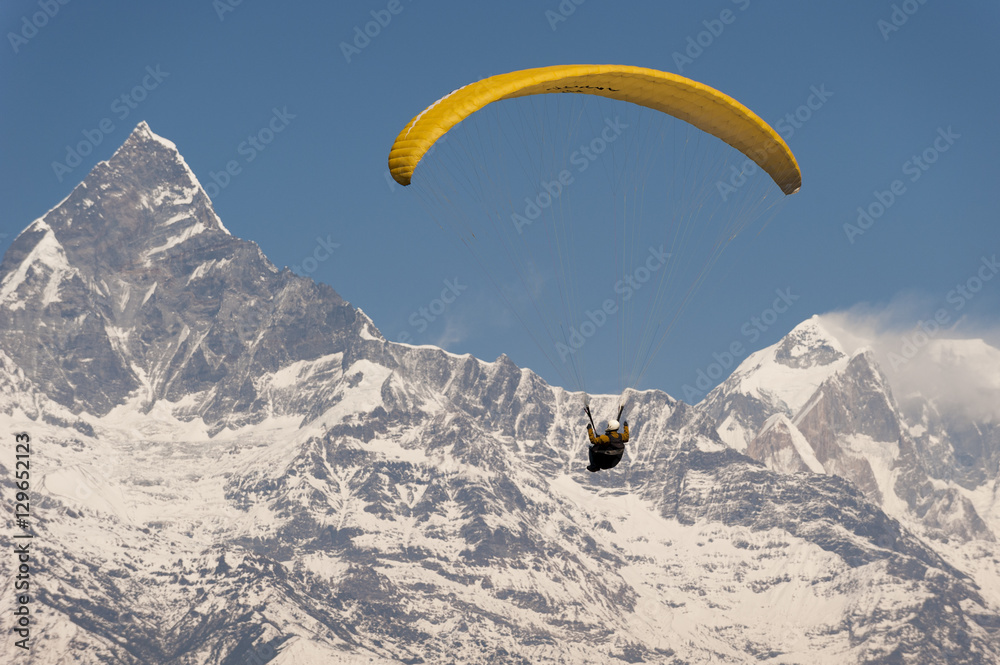 A paraglider carves a turn with views of Machapuchare (Fishtail mountain) in the distance, Nepal, Himalayas A paraglider carves a turn with views of Machapuchare (Fishtail mountain) in the distance, Nepal, Himalayas