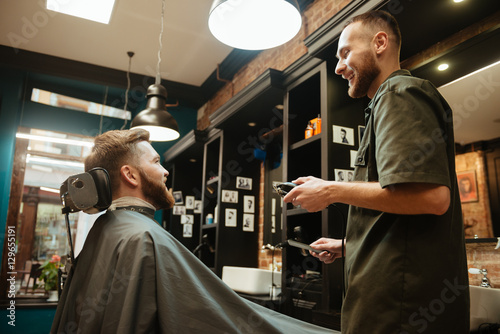 Happy man getting haircut by hairdresser with electric razor