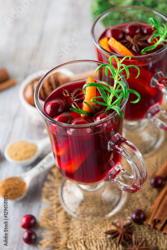 Christmas Hot mulled wine in glasses with orange slices, cranberry, anise and cinnamon sticks on white rustic wooden background, selective focus. Winter Holiday time concept
