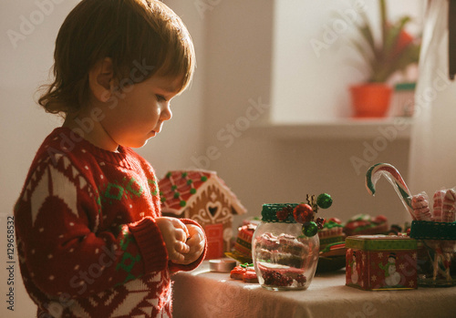 small and cute girl in a red sweater stands near Christmas cooki