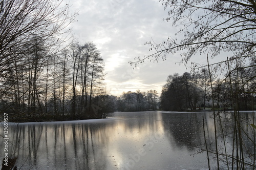 Wintersonne linst durch Wolkendecke am winterlichen See