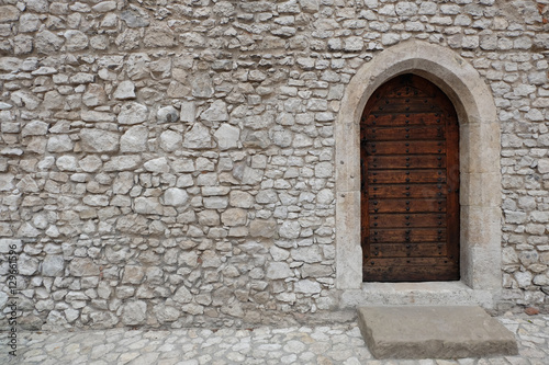 Heavy closed wooden door with pointed arch in the white cobble stone wall of a medieval fortress  made of riveted wood planks