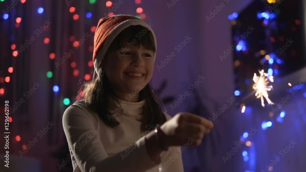 Young girl wears in sants hat having fun with sparkler Young girl wears in sants hat having fun with sparkler