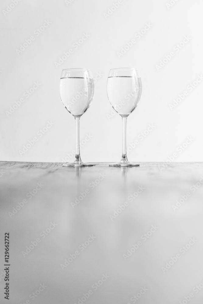 Obraz premium Two wine glasses filled with clear liquid on a wooden table