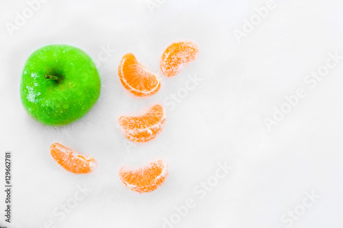 Green apple and slices of tangerines in the snow. Beautiful winter composition.