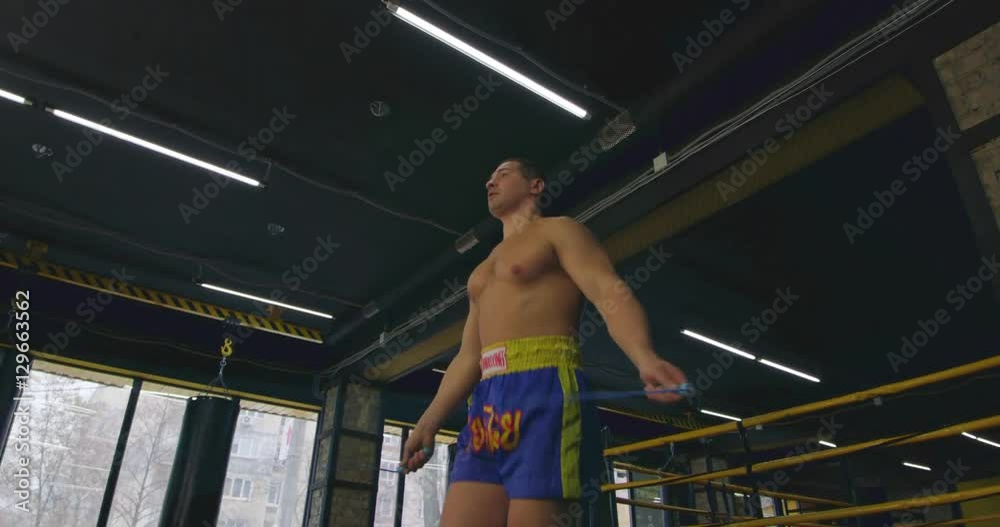 Boxer jumping rope near boxing ring 4k video. Sport skipping athletic stretch training. Bottom view of sportsman, punching bag in background Boxer jumping rope near boxing ring 4k video. Sport skipping athletic stretch training. Bottom view of sportsman, punching bag in background