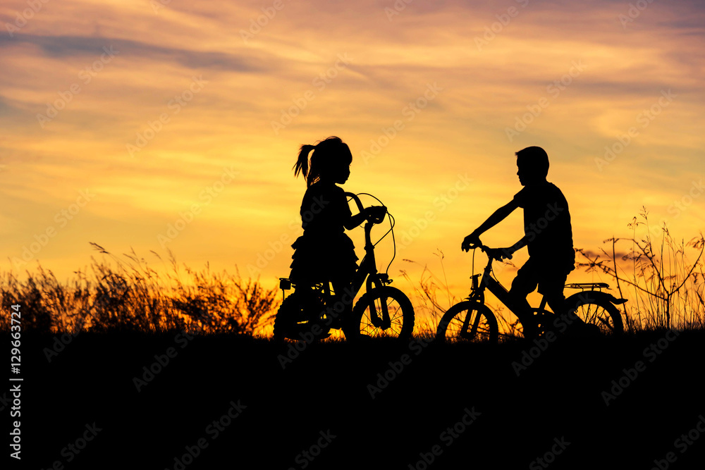   silhouette little boy and little girl  having fun riding bike on sunset  