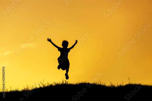 silhouette happy little girl jumping to sky on sunset