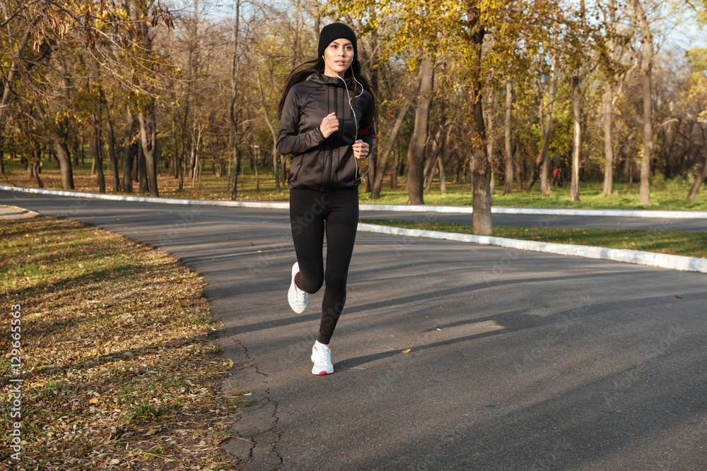 Young lady in warm clothes and earphones running Young lady in warm clothes and earphones running