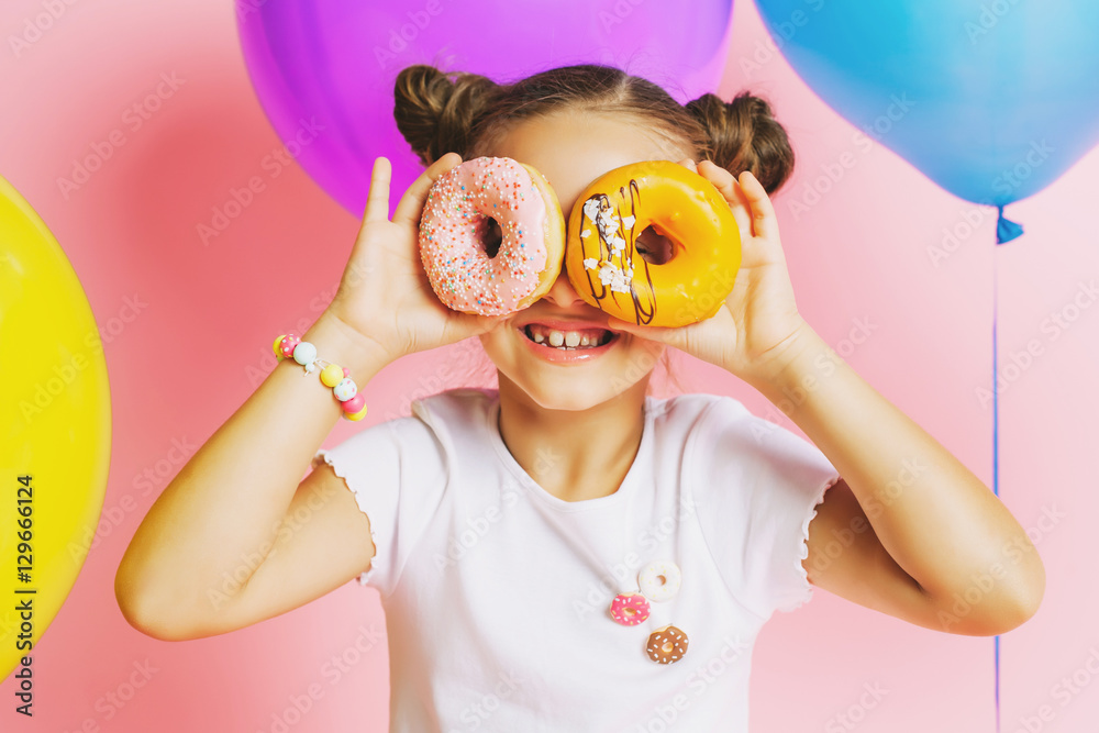 Little girl with bright balloons and donuts on a pink background