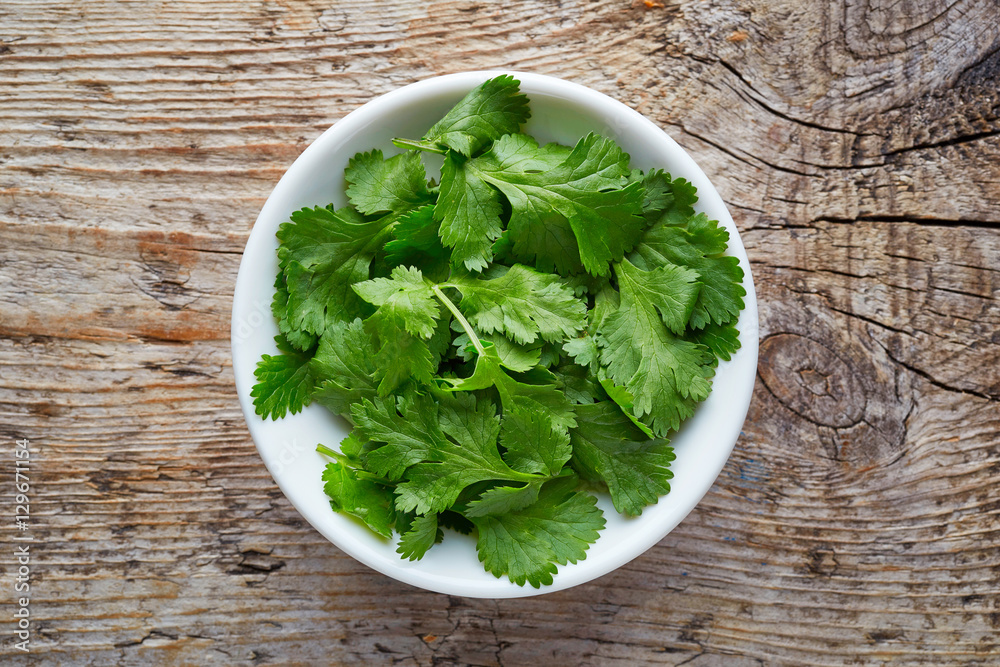 Bowl of coriander leaves on wooden table, from above Bowl of coriander leaves on wooden table, from above