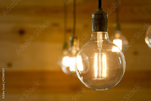 Closeup image of a turned on light bulb over a wooden background.