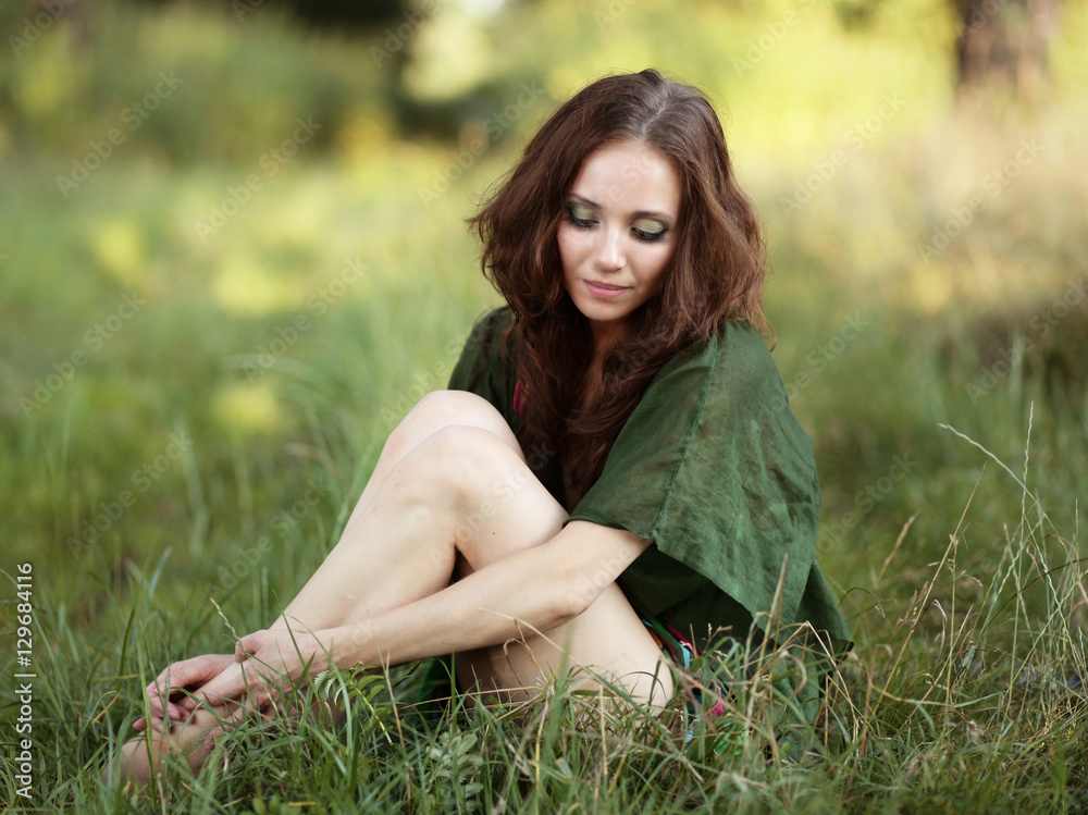 Fototapeta premium Kobieta w zielonej sukience siedząca na trawie