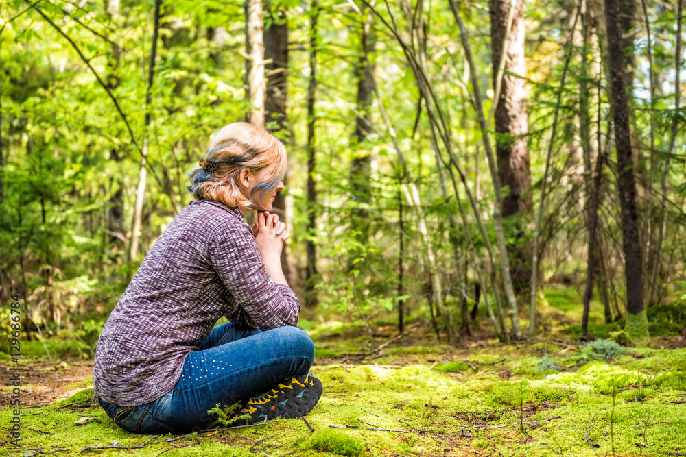 Fototapeta premium Młoda kobieta siedzi na omszałej ziemi w leśnym myśleniu