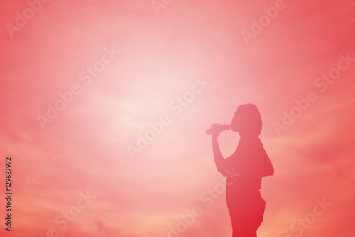 Silhouette women drinking water after running at the sky sunset, color of vintage tone 