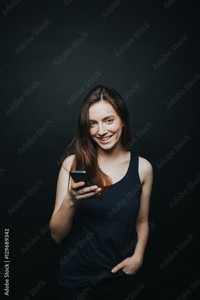 Studio shot of young beautiful brunette in black top posing with device isolated on black background. Studio shot of young beautiful brunette in black top posing with device isolated on black background.