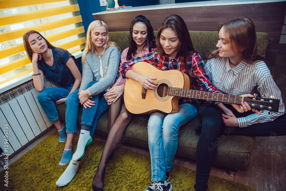 Obraz premium Beautiful girls sitting on couch, have fun and play the guitar in Hostel.