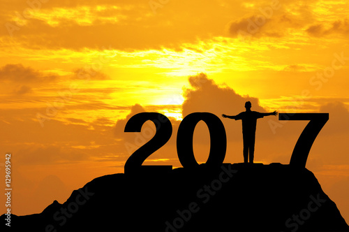 Silhouette of a man open hands on top of mountain during sunset to complete 2017 year.