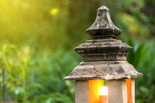 stone lantern lamp with light bulb inside in the green garden forest environment