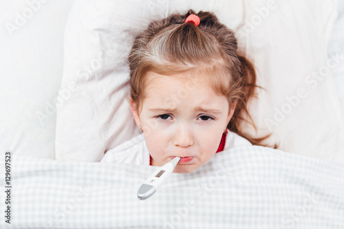 Sick girl with a thermometer in mouth lying in bed