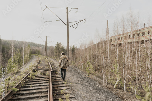 young boy walking on railroad tracks. He is holding the gun. wandering boy. man in a protective cloak with a hood. Post apocalypse. traveling on foot in a post-apocalyptic world.
